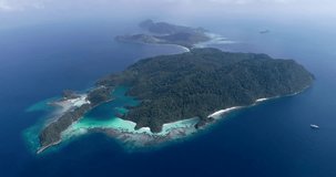 Drone footage of Raja Ampat, Indonesia with a liveaboard boat along islands covered in tropical vegetation, secluded white sand beaches and colorful shallow coral reef near Pulau Fam or Pam. The camer