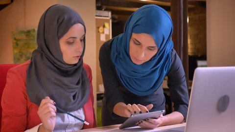 Closeup portrait of two young muslim businesswomen discussing a work topic in front of the laptop. Employer guiding the new office worker that appeared to make mistakes in her project
