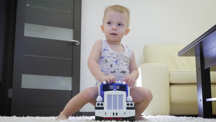 Lovely baby boy playing with a big car toy on floor at home. Kid boy toddler playing with toy car indoors. Future driver. Funny toddler boy indoors.