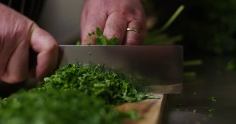A chef chopping parsley in a kitchen.