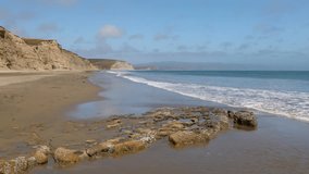 Seamlessly looping footage features Pacific Ocean waves breaking gently on the beach with tall bluffs lining the coast at Drake’s Bay at Point Reyes National Park, California.