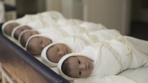 Newborn babies lying in row on table at maternity ward.The first child in focus looking around and yawning, other infants in the blurred background. Daylight.