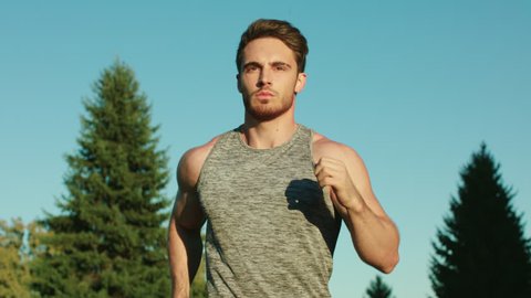Sport man running in park on blue sky background. Male runner run in park at morning. Young man training run in slow motion. Cardio exercise at workout outdoor