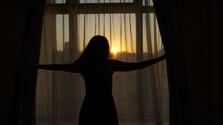 Woman open dark curtains and look to neat sunrise at early hour, black half length silhouette of slender lady against window. She stretch out hands to unveil hangings, slowly and unhurried mood at day Royalty-Free Stock Footage #1024192100