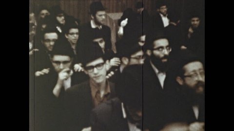 1970s: Rabbi claps hands and congregation sings. Jewish men dance and sing in synagogue. Men clap and dance in synagogue.