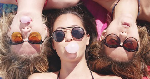 Top view of three teenage girl friends lying on back blowing bubblegum candy bubbles on beach