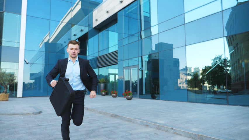 Young businessman with briefcase runs and looks at his watch. Confident guy late for meeting. Successful man in suit runs near modern building. Handsome man in hurry to appointment. Slow motion Royalty-Free Stock Footage #1024210319