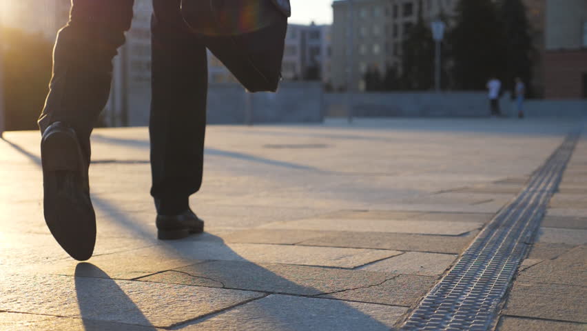 Feet of businessman with briefcase walking in city street at sunset time. Businessman commuting to work. Confident guy being on his way to office. Worker going outdoor. Rear Back view Close up Royalty-Free Stock Footage #1024210334