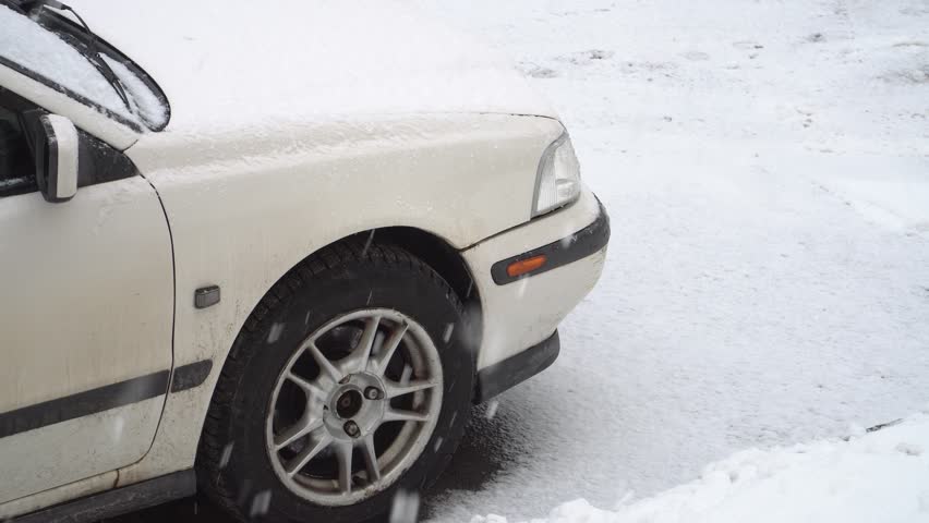 Car in the yard of the house during the winter season. Snowflakes are slowly falling down. Winter weather scene with the automobile.