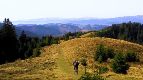 Two bikers riding down a mountain trail in autumn sunny day. Cross country biker. MTB bike riding on track trail. Riding their mountain bikes along the trail on the mountains. Enduro Trails. Aerial 
