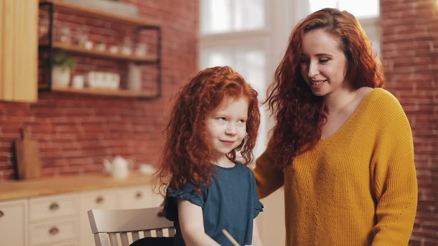 A mother and her daughter painting Easter eggs in cozy kitchen. They laughing and have fun. Happy family preparing for Easter. Happy easter