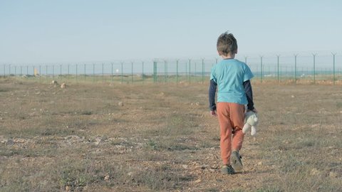 view from the back of juvenile child leaving moving towards Mexican border. Unhappy Abandoned Lonely boy walk with her Friend Teddy bunny Toy desert terrain on the state border. concept Poor Children