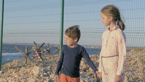 concept of two poor refugee children standing by the sea in war conflict zone. boy and girl waiting to be rescued