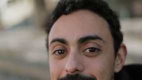 Front view of young Arabic handsome mans face with dark beard looking at camera, smiling. Close up shot. Lifestyle concept