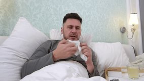Medium shot of sick man blowing his nose and talking on video call while resting in bed