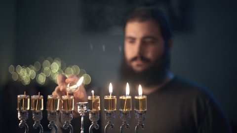 orthodox jewish man light a hanukkah menorah with olive oil candles.