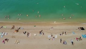 Aerial view of the beach filled with people on a hot sunny day. People rest and enjoy on the beach on a summer day near the sea ocean. 4K video.