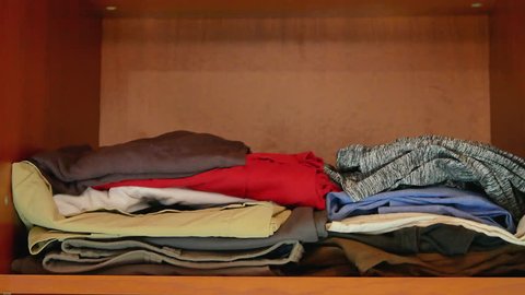 decreasing amount of clothing at wardrobe. man decluttering removing piles of clothes from shelf in closet and putting back only essential wear. minimalism konmari method concept