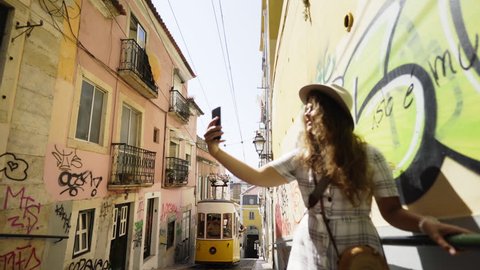 Side view of young tourist with smartphone taking selfie near retro tram on rails in Lisbon