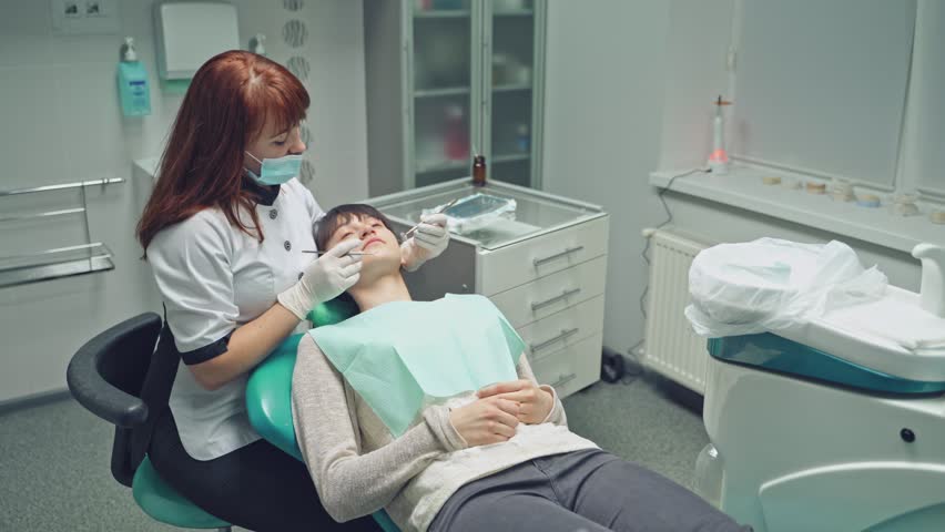 Woman patient on the inspection of the teeth in dentistry. Female dentist treats a girl's teeth in a light clean dental clinic | Shutterstock HD Video #1024256753