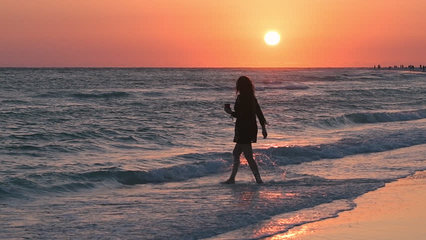 Slow motion of dreamy pink orange sunset in Sarasota Siesta Key, Florida with coastline coast of Gulf of Mexico ocean waves crashing washing on beach shore, people woman silhouttes walking entering