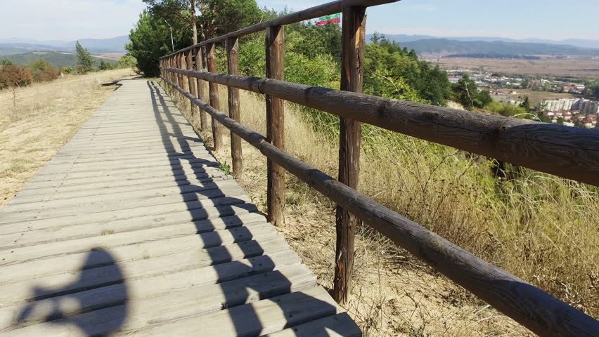 Walking on wooden walk way with fence at mountain park, pov