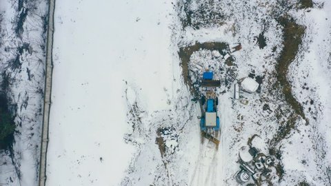 Aerial top view of a snow-clearing vehicle rakes snow on a country road
