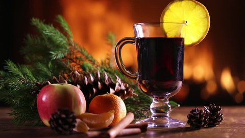 A glass of mulled wine (hot wine) with fruit and pine branches on the background of a burning fireplace
