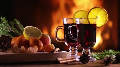 Two glasses of mulled wine (gluhwein) and a plate of fruit on the background of a burning fireplace
