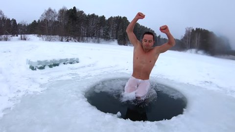 Young man jumps into the ice hole and haves recreational winter swim with joy