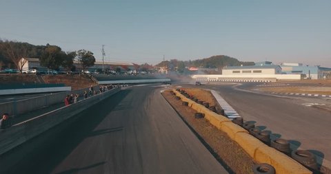 Dynamic Aerial Tracking Shot as Race Cars Speed Past Underneath Before Drifting Around a Curve.