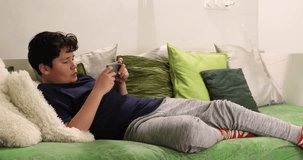 Portrait of a preteen boy with smartphone sitting on sofa at home. Kid watching to screen, reading, typing, playing games. Technology, internet communication and people concept, Smartphone addiction