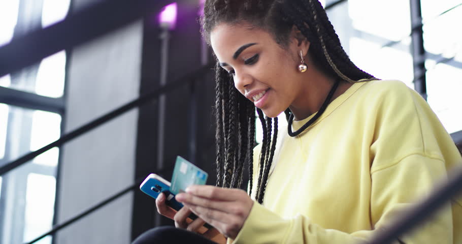 In a modern building office lady african ethnic order something online using her smartphone at the end she gesticulating with hand that she getting what she wants