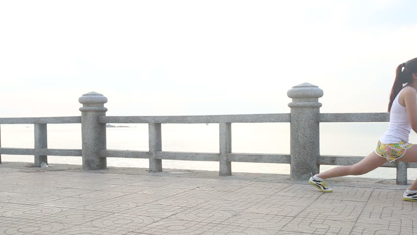 asian brunette girl does morning exercises on embankment at dawn