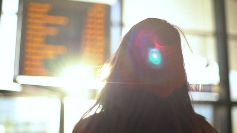 Slow motion rear-view behind charming european girl study departure board airport, train station, searching flight, sun shining camera, turning back smiling silly cute, excited travel foreign country