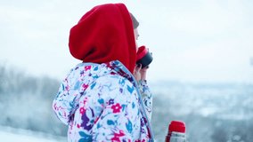 snow, winter, sport, people, beauty concept - girl pours hot tea from the thermos in the winter forest. Young woman enjoys a hot drink and smiles. ski resort