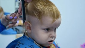 making haircut for cute 2 year old boy. cutting hair from top with scissors. handheld 4k video footage