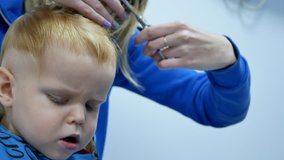 hairdresser making haircut for cute little white caucasian boy using comb and scissors. child bored and yawns. lot of empty copy space on right side. handheld 4k footage