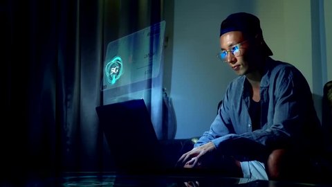 Futuristic network concept. Technology. Digitization of information flows. 5g or 4g internet speed. Young handsome asian man in glasses with reflections using his laptop, sitting in the evening in the
