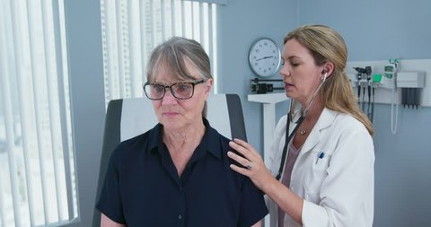 Female doctor using stethoscope listening to senior patients lungs. Older woman visiting her primary care physician for a regular check up. Slow motion 4k