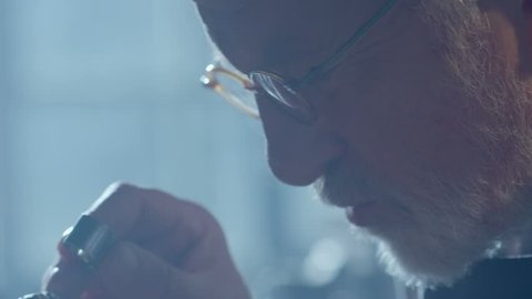 Footage of goldsmith working at table in workshop . Bearded old man jeweler creating new jewelry . Master goldsmith working process . Scenic film shot in vintage style. Shot on RED EPIC Camera.   