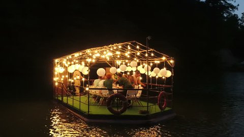 Young people or friends are partying on the little cafe ship . Beautiful restaurant ship with festoon , bulb lights on the lake at the nature . Areal flying view of beautiful boat on the lake .