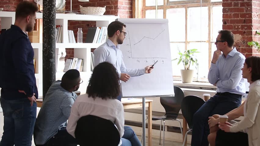 Confident speaker coach gives corporate presentation on whiteboard teaching diverse sales team at group meeting, male business trainer presenter speaking at training explaining report graph in office Royalty-Free Stock Footage #1024307081