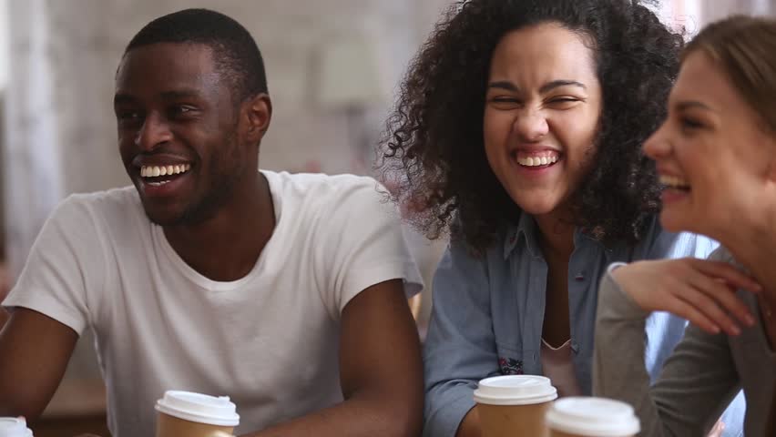 Happy multiracial young people friends talking laughing at group meeting sharing cafe table, diverse students drinking coffee having fun together enjoy multi-ethnic friendship pleasant conversation