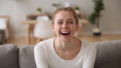 Happy teen girl laughing out loud at humorous joke looking at camera at home, cheerful casual young woman with funny face sit on sofa enjoy sincere positive emotions screaming with laughter concept
