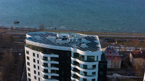 Solar panels on top of a green energy apartment building's roof. Aerial shot of elegant highrise by the sea