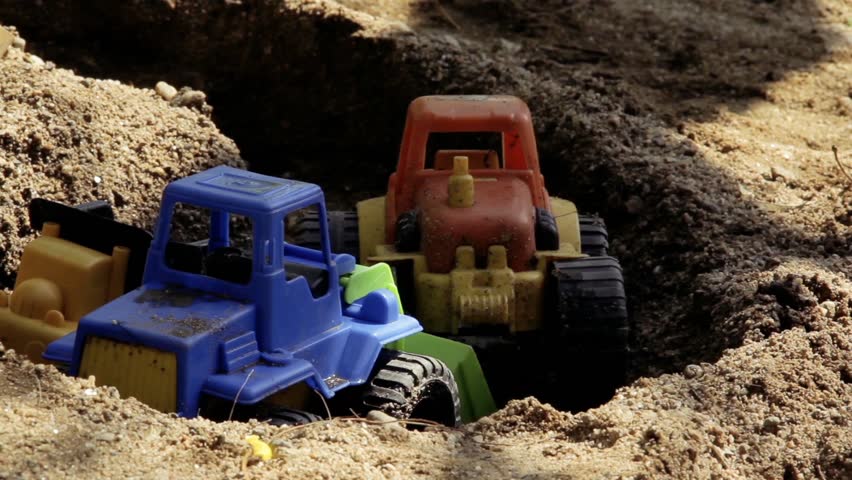 Plastic Toy Tractors Abandoned in a Sandbox. Close Up.
