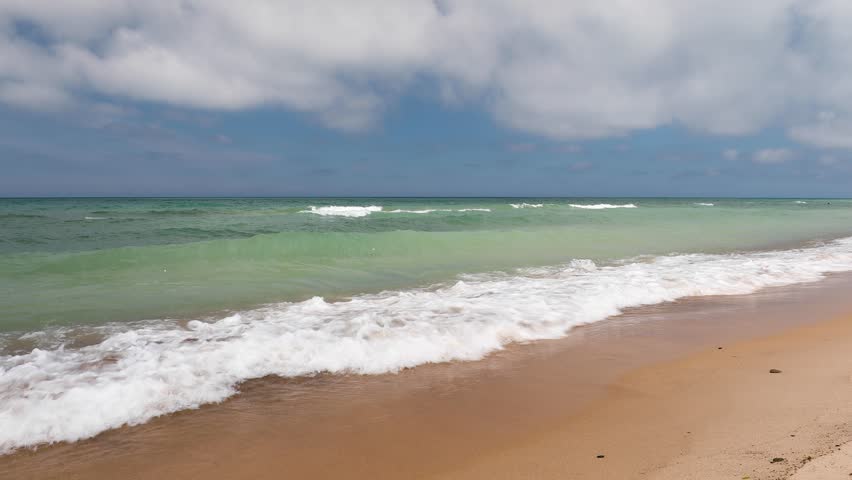 This footage features and absolutely gorgeous afternoon on a Lake Michigan beach with waves breaking gently on the sand and beautiful colors in the water and a cloudy sky over the Great Lake.