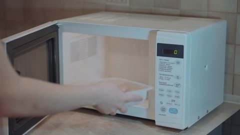 Heated food in the microwave. Female hand puts pies in the microwave in the lunch box. Cooking in the microwave. 4k video.