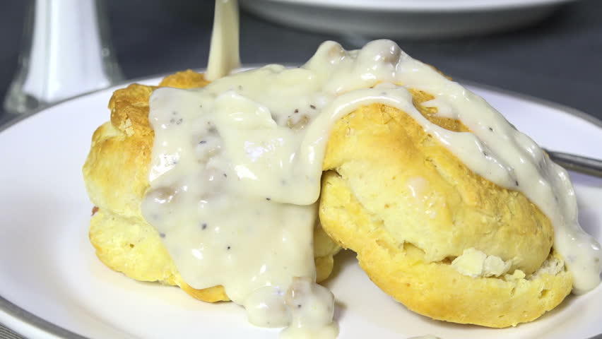 Spooning country gravy with sausage on biscuits slow motion